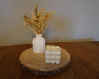 Peut inclure: Un vase en céramique blanche avec une surface texturée contient un bouquet de fleurs séchées avec des accents dorés. Une bougie à bulles blanche repose sur une tranche de bois.