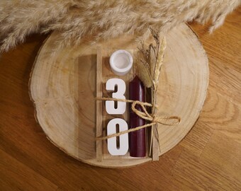 Peut inclure: Un support rectangulaire en bois contient les chiffres 3 et 0 en blanc, un petit bougeoir circulaire blanc et une bougie pilier bordeaux foncé. Les éléments sont attachés avec de la ficelle et ornés d'un bouquet d'herbes séchées beiges.