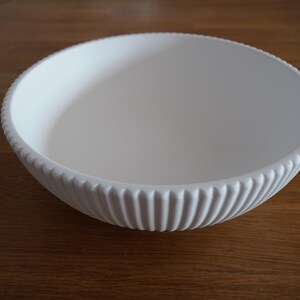 May include: A white ceramic bowl with a ribbed design. The bowl is empty and sitting on a wooden surface.