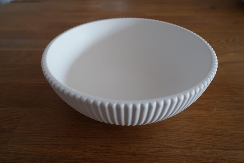May include: A white ceramic bowl with a ribbed design. The bowl is empty and sitting on a wooden surface.