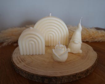 Peut inclure: Un ensemble de quatre bougies en cire blanc cassé comprenant deux formes d'arc-en-ciel de tailles différentes, une bougie en forme de rose et une bougie en forme de gnome avec un chapeau pointu, chacune avec une mèche blanche.