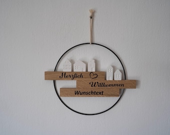 Peut inclure: Une pancarte de bienvenue en bois avec un anneau en métal noir pour l'accrocher. La pancarte a un cœur blanc et de petites maisons blanches avec le texte "Herzlich Willkommen Wunschtext".
