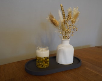 Peut inclure: Un vase en céramique blanche à texture côtelée contient un bouquet de fleurs séchées aux accents blancs et dorés. Un bocal en verre transparent avec une bougie blanche et des accents verts et dorés repose sur un plateau ovale gris.