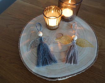 Peut inclure: Deux décorations d'ange faites à la main avec des corps en pompons macramé bleu et gris, des têtes en perles de bois et des ailes métalliques. Un ange a des ailes argentées et l'autre des ailes dorées. Chaque ornement a une boucle.