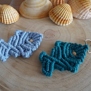 Könnte beinhalten: Zwei Makramee-Fisch-Schlüsselanhänger, einer blau und einer türkis, mit Holzperlen und einem silbernen Metallverschluss.