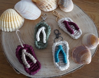 Peut inclure: Plusieurs porte-clés en forme de tongs crochetées à la main, de couleurs variées : vert, blanc, bordeaux et bleu. Les porte-clés sont présentés sur une tranche de bois avec des coquillages, évoquant un thème estival.