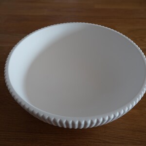 May include: A white ceramic bowl with a fluted rim. The bowl is empty and has a smooth, glossy finish.