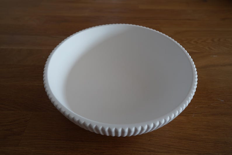 May include: A white ceramic bowl with a fluted rim. The bowl is empty and has a smooth, glossy finish.