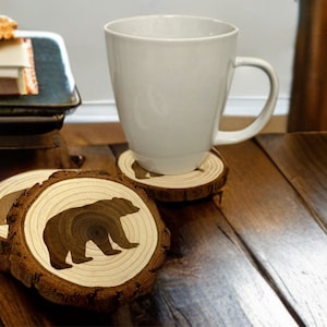 May include: Four wooden coasters with a bear silhouette design. The coasters are made of natural wood and have a rustic look.