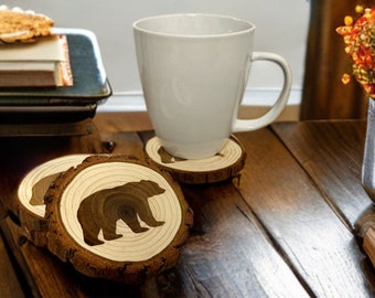 May include: Four wooden coasters with a bear silhouette design. The coasters are made of natural wood and have a rustic look.