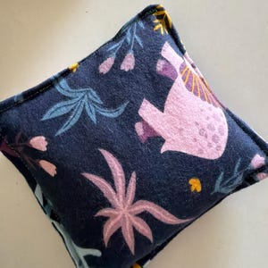 May include: A square fabric pouch featuring a dark navy blue background with a repeating pattern of light pink elephants, stylized pink and blue tropical leaves, and small yellow floral accents, finished with visible stitched edges.
