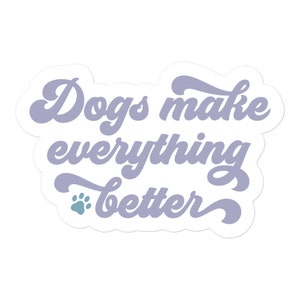 May include: A die-cut sticker featuring the text "Dogs make everything better" written in a light purple, cursive-style font. A small, solid teal-colored paw print icon is positioned to the left of the word "better" on the bottom line.