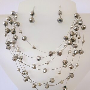May include: A multi-strand necklace featuring thin silver-toned wires adorned with faceted metallic gray beads and small smooth silver spheres, accompanied by a pair of matching drop earrings with similar faceted beads.