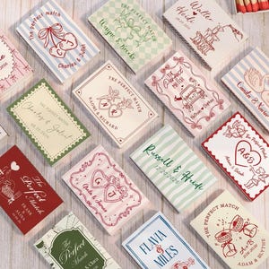 May include: A collection of rectangular matchboxes featuring various custom designs, including names, dates, and illustrations like hearts, swans, and cars. Each box displays unique patterns such as stripes or checkered prints in colours like red, green, blue, and pink.