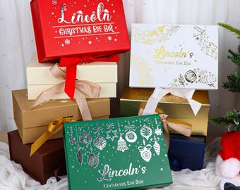 May include: A collection of rectangular gift boxes in red, cream, brown, white, gold, and green. Each box features a ribbon closure and personalized text reading Lincoln's Christmas Eve Box, decorated with silver or gold foil holiday motifs.
