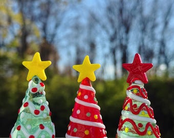 Peut inclure: Trois décorations de sapin de Noël en verre. Les sapins sont décorés de volutes rouges et blanches, de points rouges et blancs et de volutes vertes et blanches. Les sapins ont des étoiles jaunes et rouges en guise de sommet.