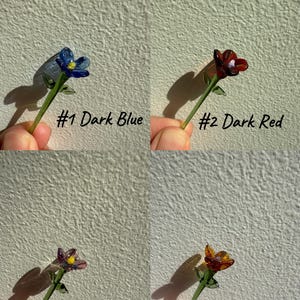 K&ouml;nnte beinhalten: Vier Glasblumen-Stiel-Ornamente in verschiedenen Farben: Dunkelblau, Dunkelrot, Hellbraun und Dunkelgelb. Jeder Stiel hat eine kleine Glasblume mit einem gr&uuml;nen Stiel und Bl&auml;ttern.