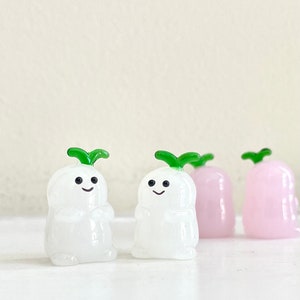 May include: Four small glass figurines of radishes. Two are white with green tops and two are pink with green tops.
