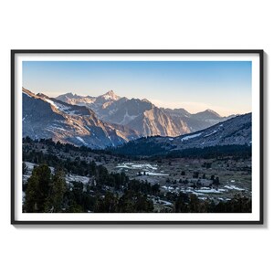 May include: A panoramic view of a mountain range with snow-capped peaks and a valley in the foreground. The mountains are a light blue color and the valley is covered in green grass and trees. The sky is a light blue color.