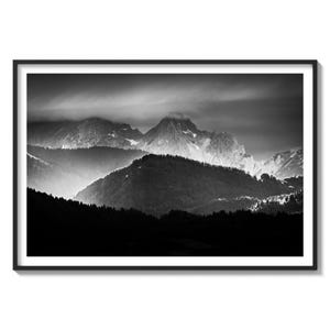 May include: A black and white photograph of a mountain range with clouds in the sky. The mountains are covered in snow and the sky is cloudy. The photo is taken from a low angle, looking up at the mountains.