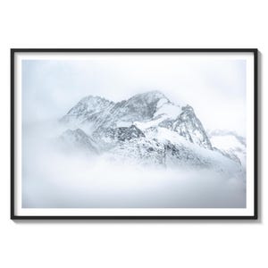 May include: A snowy mountain range with a peak covered in fog. The mountain is a light gray color and the fog is a white color.