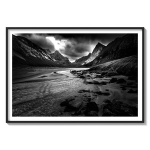 May include: A black and white photograph of a river flowing through a valley between two mountains. The river is calm and the water is smooth. The mountains are tall and imposing, and the sky is cloudy.