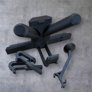 Puede incluir: Un conjunto de componentes negros impresos en 3D, que incluyen una estructura central con brazos cilíndricos, varios clips en forma de gancho y una pieza única en ángulo con un extremo circular. Fondo gris.