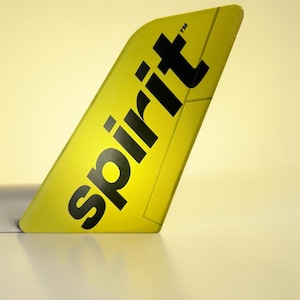 May include: A yellow airplane winglet with the word "spirit" in bold black letters. The winglet is angled, with a white surface below and a soft yellow background.