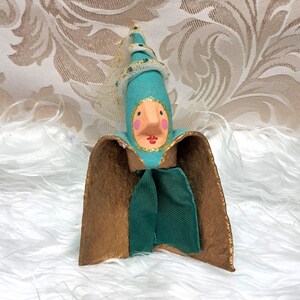 May include: A whimsical paper mache figurine with a teal hat, gold cape, and green sash. The figurine has a painted face with pink cheeks and red lips.