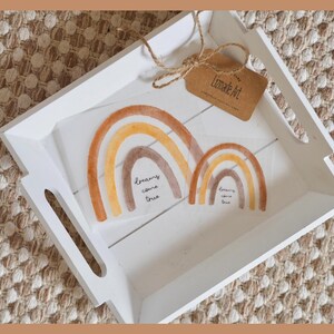 Könnte beinhalten: Ein weißes Holztablett mit ausgeschnittenen Griffen enthält zwei Aquarell-Regenbogen-Kunstdrucke. Die Regenbogen sind in Braun-, Orange- und Gelbtönen gehalten. Der Text "dreams come true" ist auf die Drucke geschrieben. Ein Etikett mit dem Text "Lizmade Art" ist angebracht.