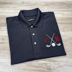 May include: Black golf polo shirt with a red embroidered monogram "C B" and crossed golf clubs with a golf ball.