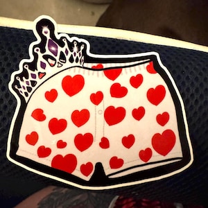 May include: A sticker featuring a pair of white underwear adorned with red hearts. A black and white crown is at the top. The underwear has a black border and a dotted line down the center.