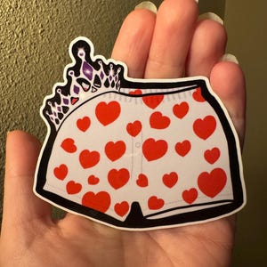 May include: A sticker featuring a pair of white underwear with red heart patterns. A black outline frames the underwear, and a purple and silver crown is above the underwear.
