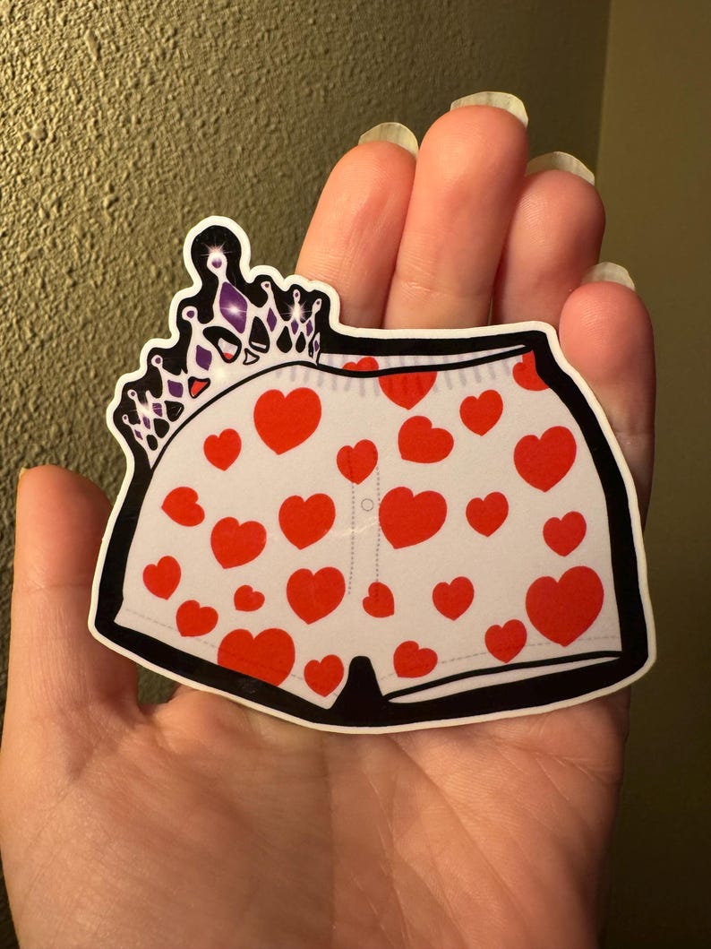May include: A sticker featuring a pair of white underwear with red heart patterns. A black outline frames the underwear, and a purple and silver crown is above the underwear.