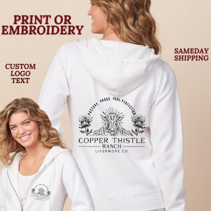 May include: White hooded sweatshirt with a black and white logo on the back that says "Copper Thistle Ranch Livermore Co." The logo features a cow's head with a sunburst and two flowers.