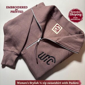 May include: A mauve zip-up sweatshirt with a silver zipper and black embroidered text. The sweatshirt has a hood and pockets. The text "WIC" is embroidered on the front. The text "Embroidered or Printed" is at the top.
