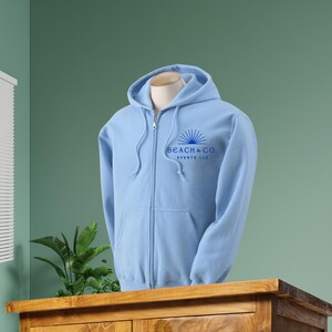 May include: A light blue zip-up hoodie with a blue logo that says "Beach & Co. Events LLC" on the front.