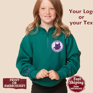 May include: A teal quarter-zip sweatshirt with a purple and white patch featuring a cartoon fox and the text "Purple Foxes." The sleeve has embroidered initials. The image also includes the text "Your Logo or your Text."