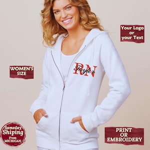 May include: White zip-up hoodie with a hood and pockets. The hoodie features the letters "RN" in red with the name "Layla" in a script font. The hoodie is a women's size and can be printed or embroidered.