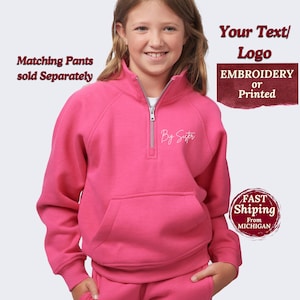 May include: A bright pink zip-up sweatshirt with a front pocket and the text "By Sister" in white script. The sweatshirt has a silver zipper and is part of a set, with matching pants sold separately. The image also includes text that says "Your Text/Logo EMBROIDERY or Printed".