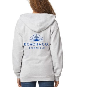 May include: A pale grey hooded sweatshirt with a blue logo that reads "BEACH & CO. EVENTS LLC". The logo features a sunburst design. The sweatshirt has a drawstring hood and a full zip.