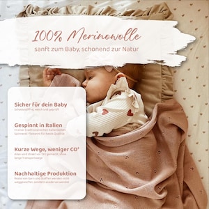 May include: A baby sleeping on a beige ruffled pillow and covered by a dusty pink knit blanket with a small eyelet pattern. The image includes text in German: 100% Merinowolle, sanft zum Baby, schonend zur Natur, Sicher f&uuml;r dein Baby, Gespinnt in Italien, Kurze Wege, weniger CO2, Nachhaltige Produktion.