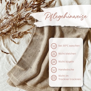 May include: A beige knit blanket with a delicate pointelle pattern. A white rectangular care instruction card is overlaid, featuring the text Pflegehinweise and five icons with German text: bei 30&deg;C waschen, Nicht bleichen, Nicht b&uuml;geln, Handw&auml;sche, and Nicht im Trockner trocknen.