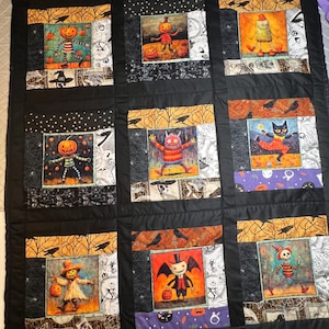 May include: A Halloween-themed quilt with nine square panels. Each panel features a unique, colorful illustration of spooky characters like scarecrows, pumpkins, and monsters. The quilt is bordered by black fabric and stitched together with black thread.