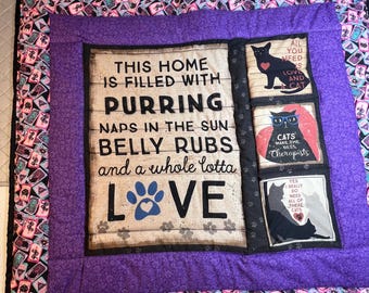 May include: A quilted throw blanket with a purple center and a patterned border. The center features a wooden-style sign with the text "THIS HOME IS FILLED WITH PURRING...LOVE." Additional panels display cat-themed graphics and text, including "Cats make the best therapists."