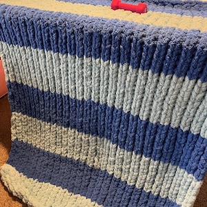 May include: A blue and light blue striped knitted blanket with a chunky knit texture.