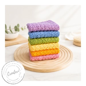 Könnte beinhalten: Ein Stapel aus sechs rechteckigen, gehäkelten Waschlappen in einem lebendigen Regenbogenverlauf mit texturiertem Stichmuster. Die Farben von oben nach unten sind Lavendel, Blau, Grün, Gelb, Orange und Pink, ordentlich gefaltet und gestapelt.
