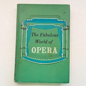Puede incluir: Un libro antiguo titulado "The Fabulous World of OPERA" con una cubierta verde. La portada presenta una ilustración turquesa y blanca de un escenario con cortinas. El título está en blanco, con la palabra "OPERA" en una fuente más grande.