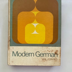 Può includere: Una copertina di libro vintage con un design geometrico in tonalità di marrone, arancione e giallo. Il titolo "Modern German" è stampato in nero su sfondo bianco, con i nomi degli autori "Vail/Sparks" stampati sotto in un carattere più piccolo.