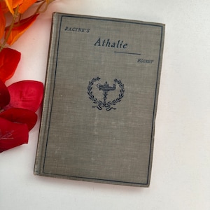 Peut inclure: Un livre vintage intitulé "Racine's Athalie" par Eggert. La couverture du livre est de couleur vert foncé avec une illustration en noir et blanc d'une couronne avec une lampe à l'intérieur.